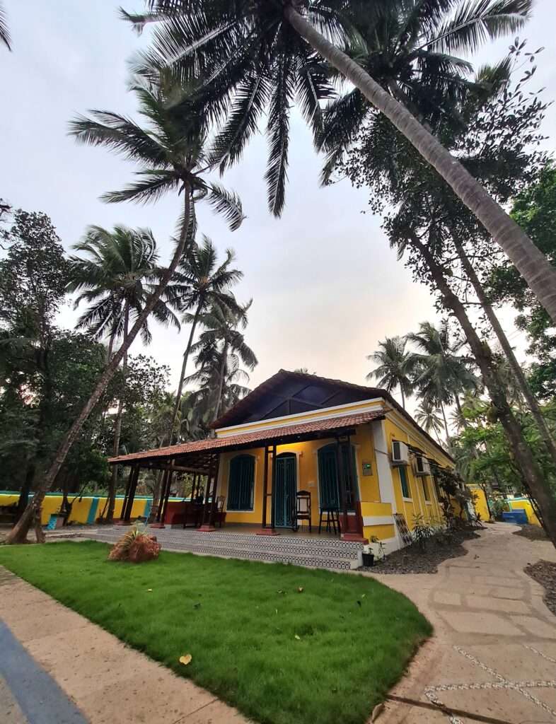 Guests enjoying sunset cocktails on the teakwood veranda at Valentine Villa, a 1924 Portuguese heritage property in Arpora - showcasing outdoor lounge, tropical plants, and vintage azulejos tiles